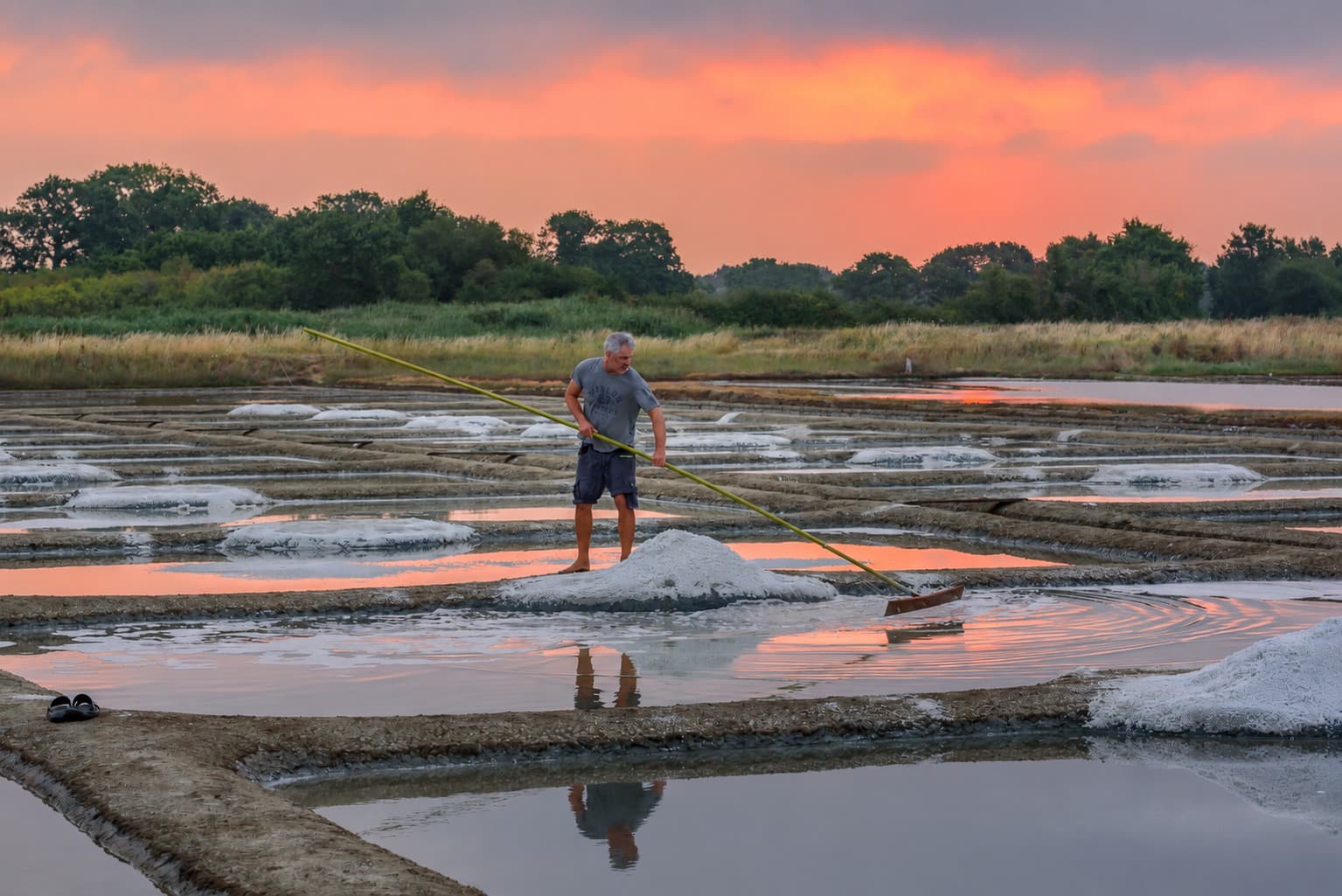 Un paludier récoltant le sel au coucher du soleil dans les marais de Guérande